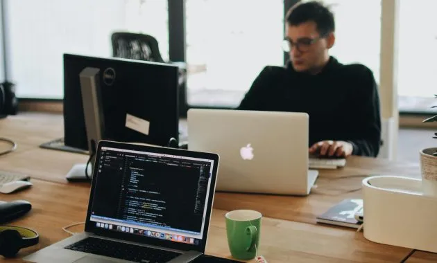 Man in Black Shirt Sits Behind Desk With Computers