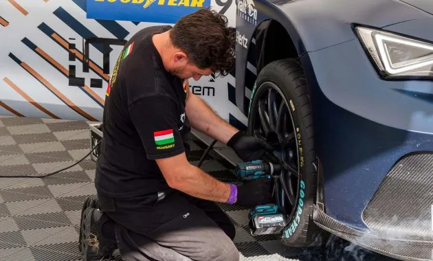 Mechanic fixing a car tire in a service station using power tools. Professional car maintenance.