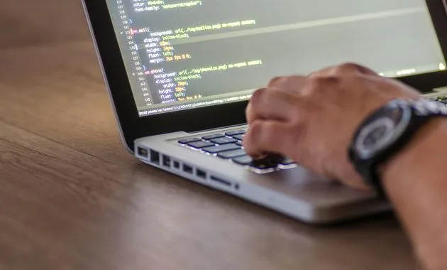 A close-up shot of a person coding on a laptop, focusing on the hands and screen.
