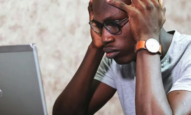 A man appears frustrated while working on a laptop in an office setting, showcasing remote work challenges.