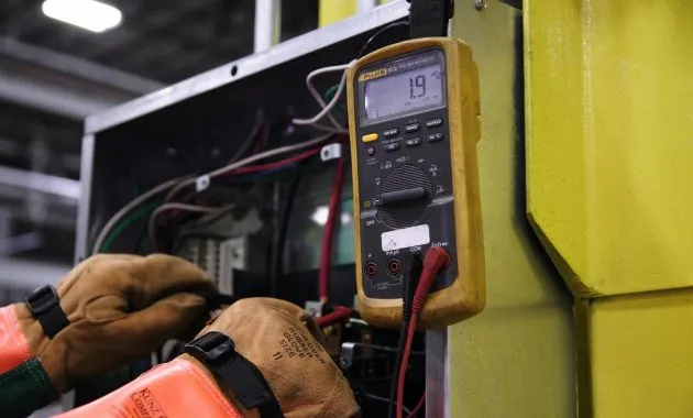 Electrician using a multimeter to fix industrial control panel wiring.